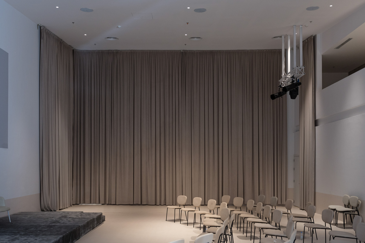 Interior performance space with floor-to-ceiling grey curtains and rows of chairs facing a stage