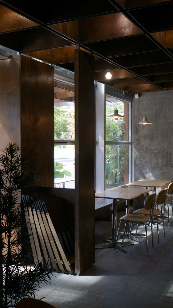 Corner seating nook with dark timber columns, potted plant, and pendant lights beside street-facing windows
