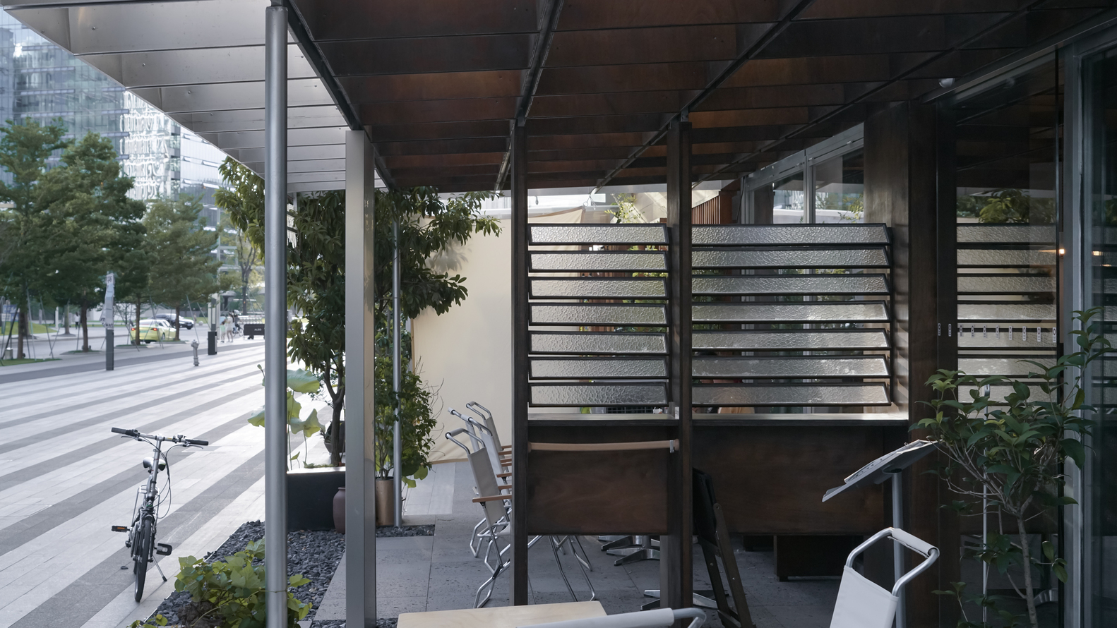 View through the open pavilion showing horizontal slatted screens and steel structural frame with pedestrians beyond