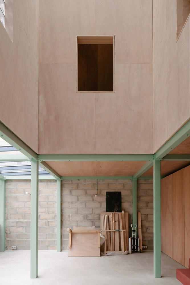 Ground floor space with pale plywood ceiling above green steel columns and concrete block walls