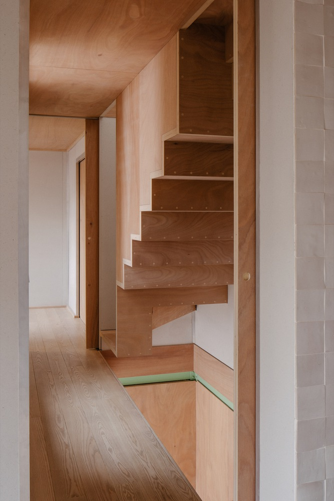 Plywood alternating tread stair rising within a corridor with green metal threshold detail
