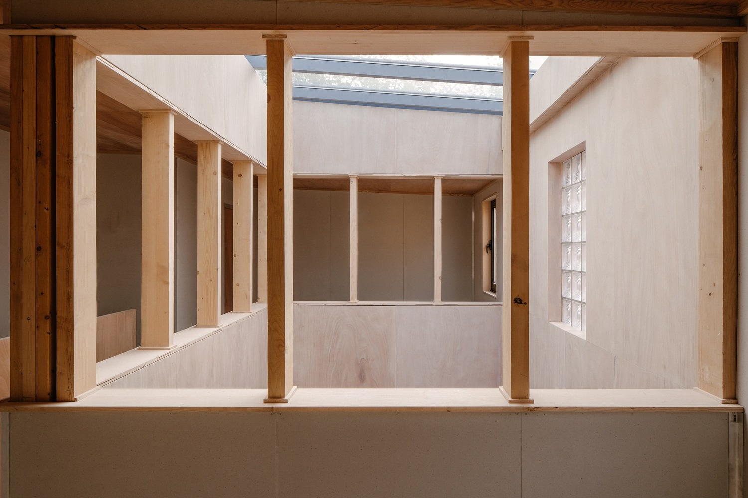 Double-height interior courtyard with plywood walls, timber columns and a linear skylight above