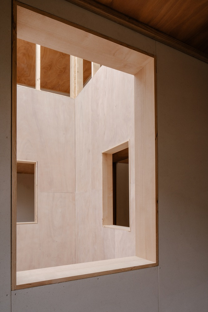 View into a plywood-lined room with clerestory windows and integrated shelving under a timber ceiling