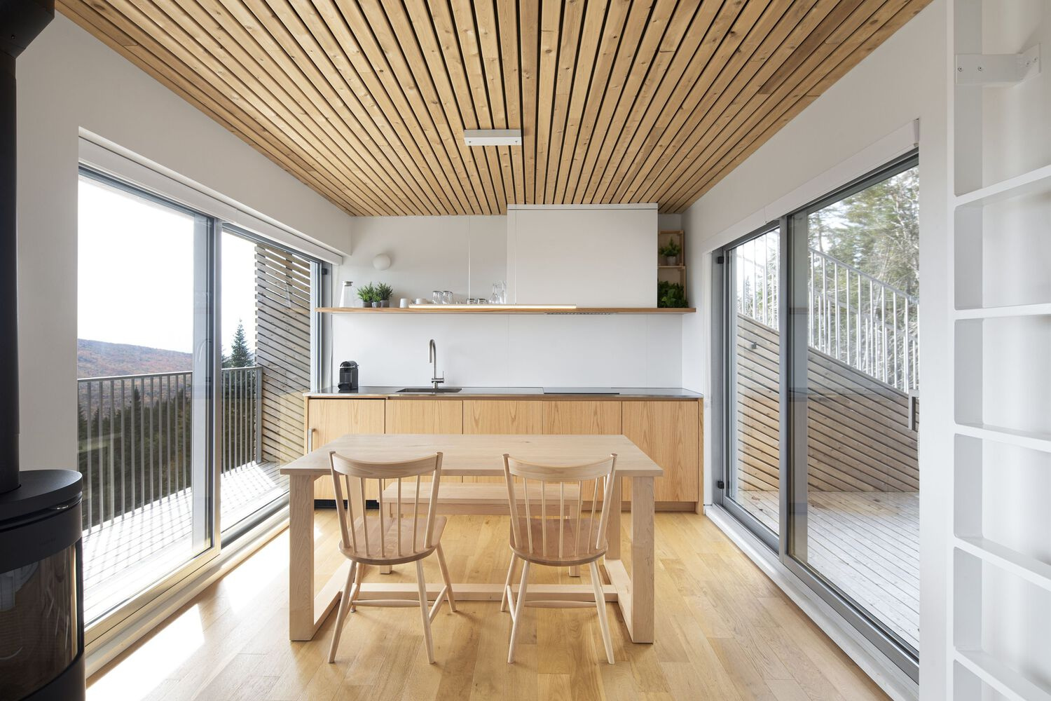 Interior dining area with slatted wood ceiling and floor-to-ceiling glazing opening to deck