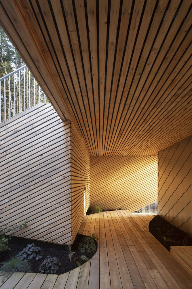 Covered terrace with angled wood-slat ceiling and walls surrounding planted beds with grasses