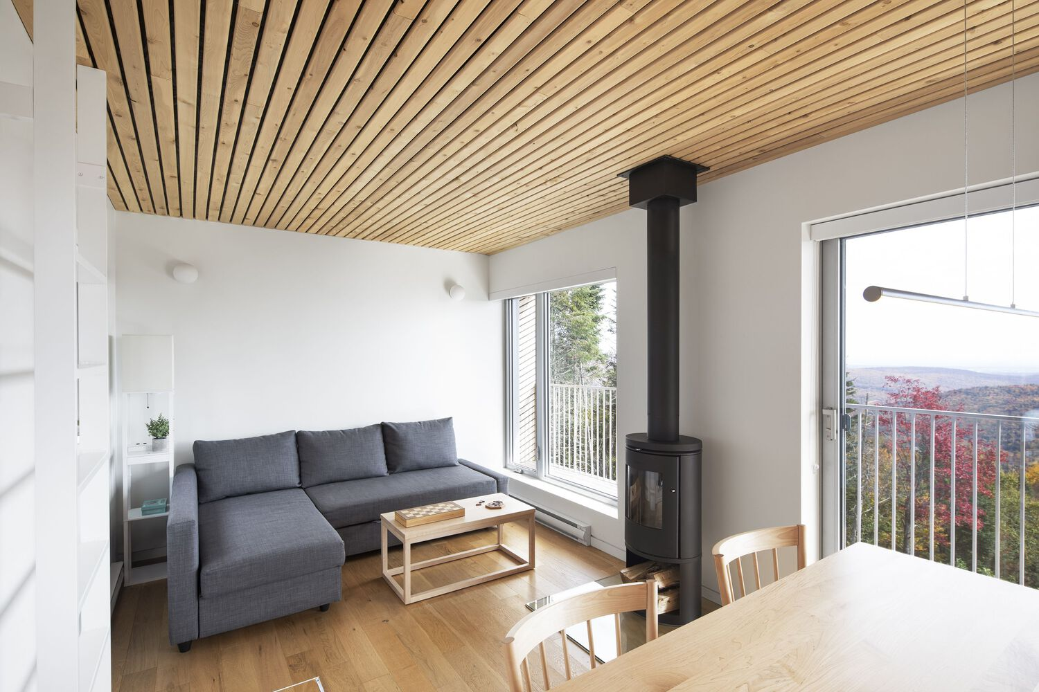 Living space with wood stove and slatted ceiling overlooking distant autumn foliage