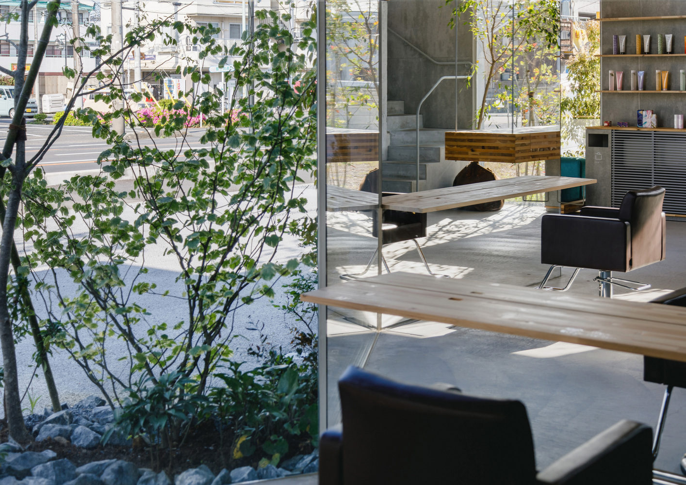 Interior view past a planted courtyard tree toward salon stations with dappled sunlight on the floor