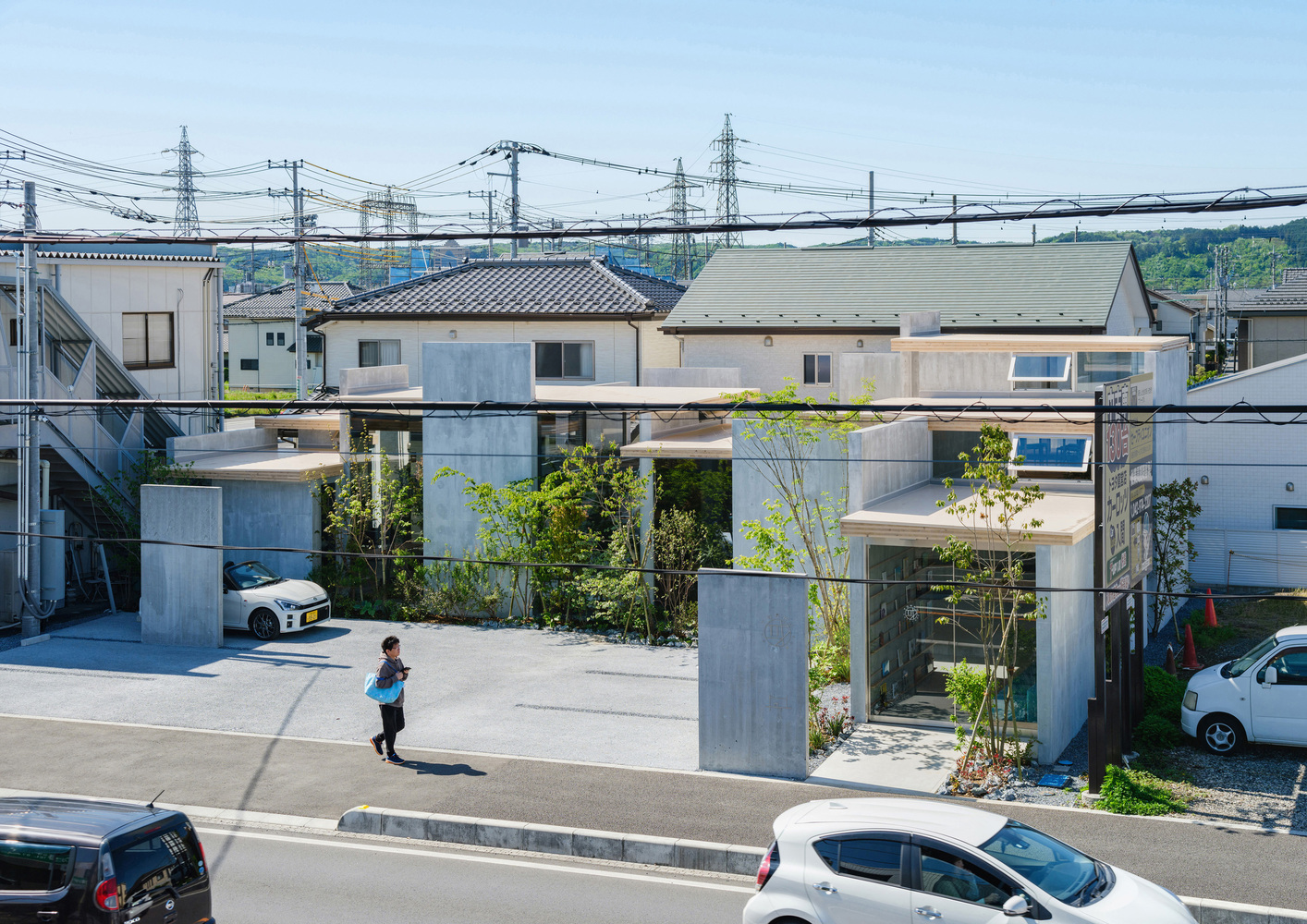 Street view of the glass-walled structure elevated on concrete columns with a child walking in the forecourt