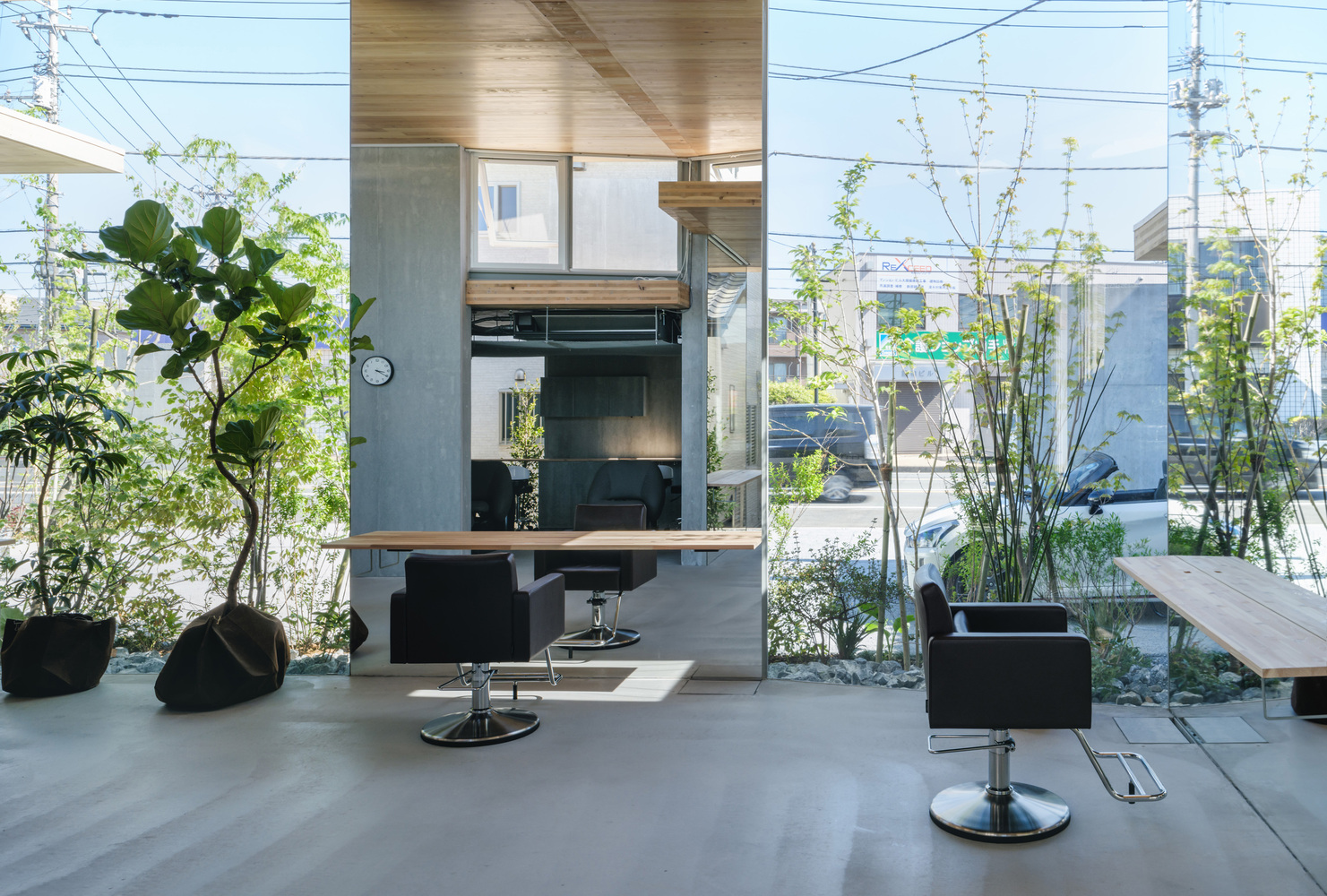 Salon chair and mirrored station framed by concrete column and glass walls opening to planted edge
