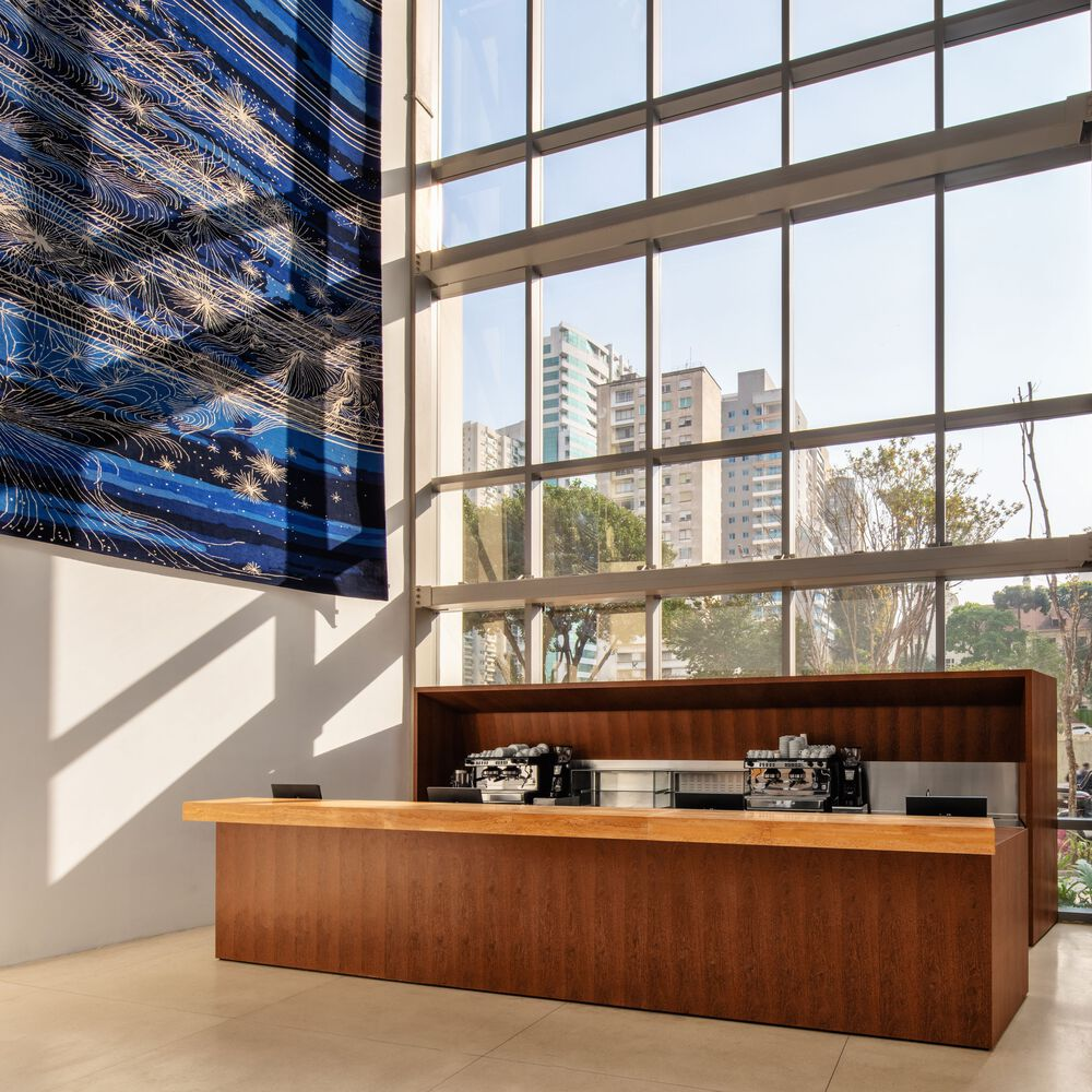 Timber service counter beneath a tall window wall with reflective metal artwork and afternoon light