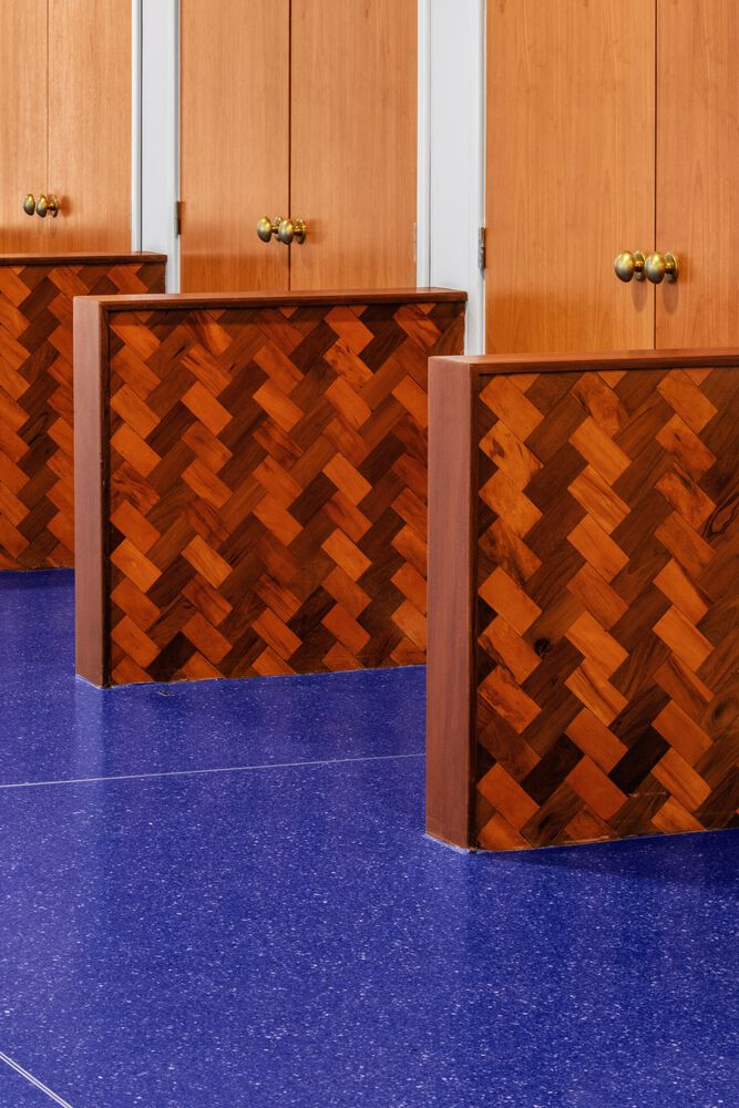 Herringbone wood veneer reception desks with brass hardware against blue carpet and vertical wood paneling