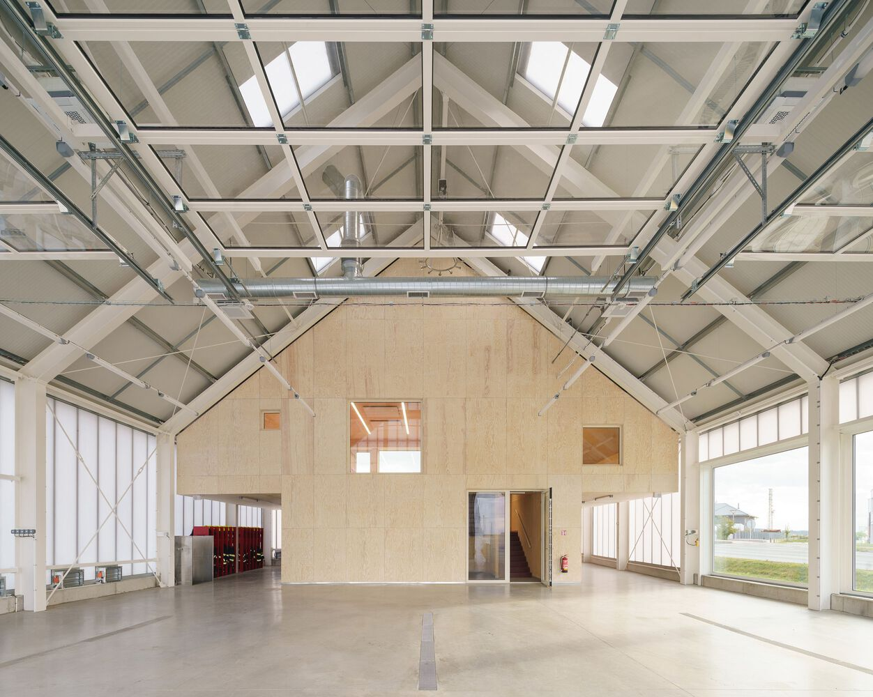 Plywood gabled training structure within large garage space with steel truss roof and skylights
