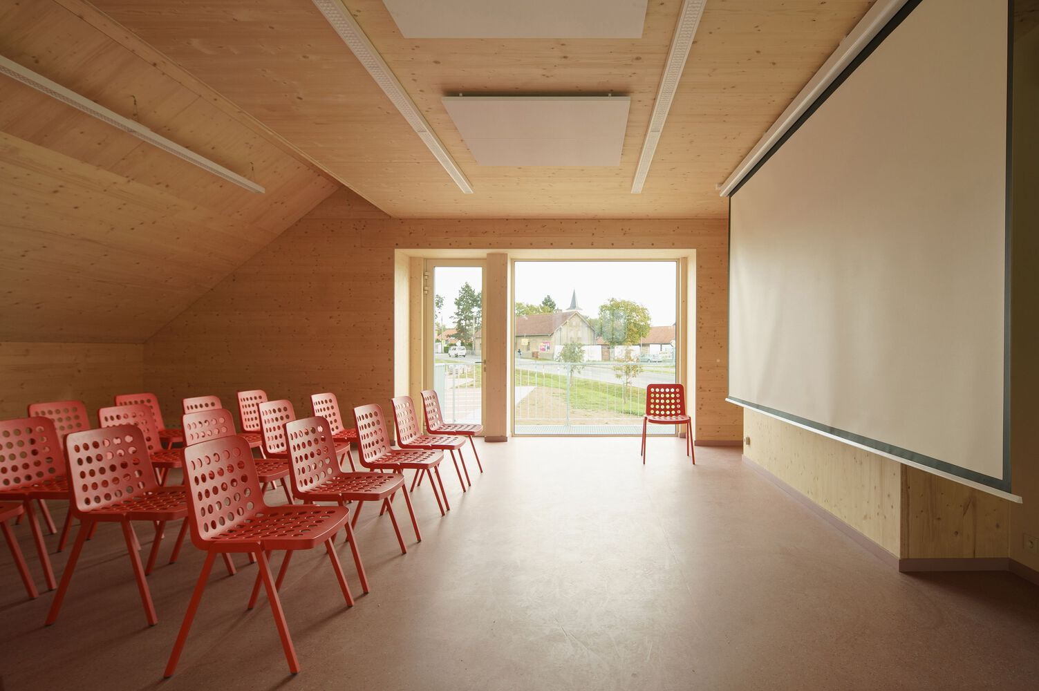 Meeting room with red perforated chairs, timber ceiling and wall panels framing window to landscape