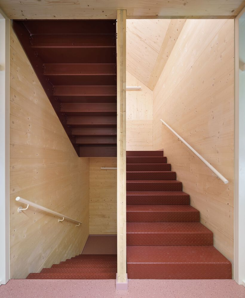 Switchback staircase with red rubber treads and pale timber wall panels under a skylight
