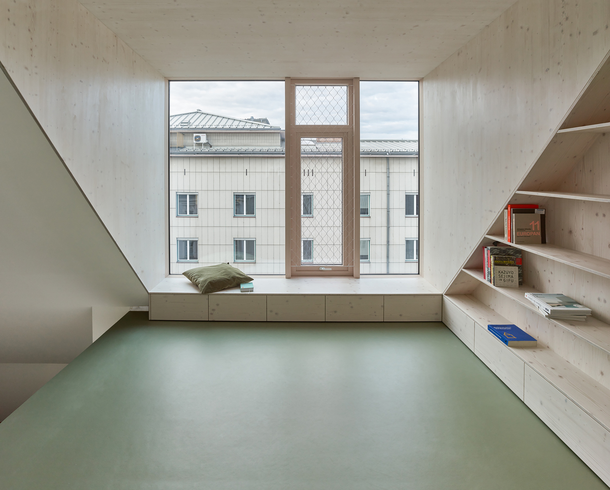 Interior room with pale green floor, built-in timber shelves and window seat overlooking neighboring rooftops
