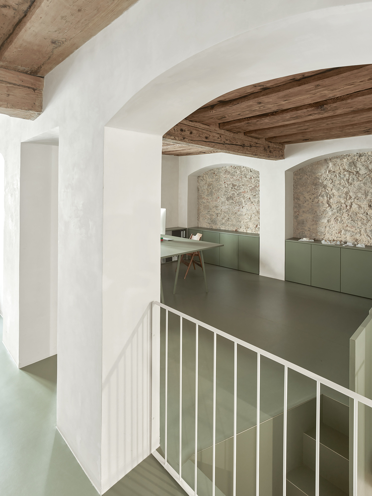 Split-level interior with exposed timber beams and olive-green cabinetry beneath textured stone arches