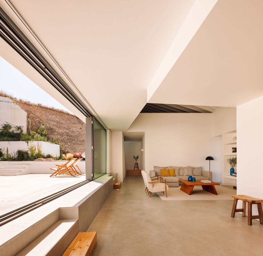 Living room with floor-to-ceiling sliding glass doors opening to a terraced courtyard with dry hillside beyond