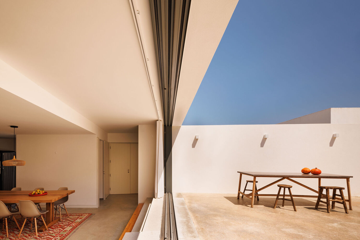 Covered terrace with fully retractable glass wall connecting interior dining area to exterior courtyard under blue sky
