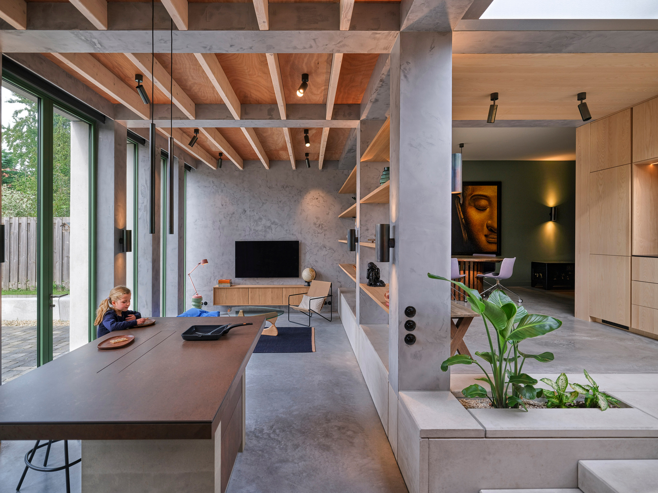 Living area with exposed timber joists, concrete columns, and planted interior bed beside dining table