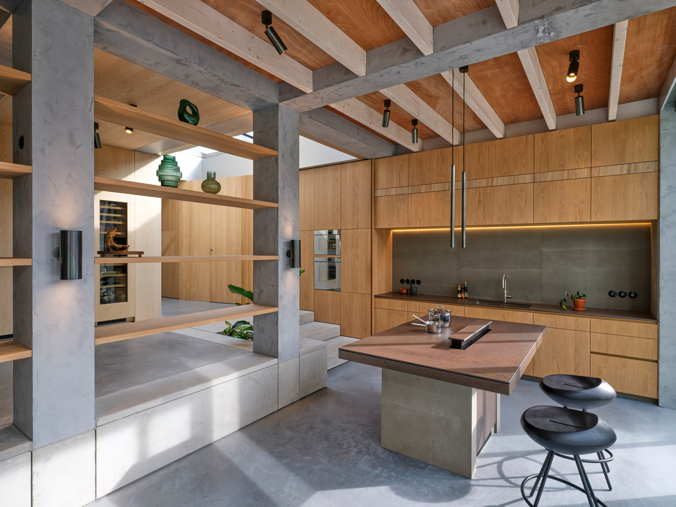 Kitchen island with walnut countertop beneath concrete beams and timber joists in open living space