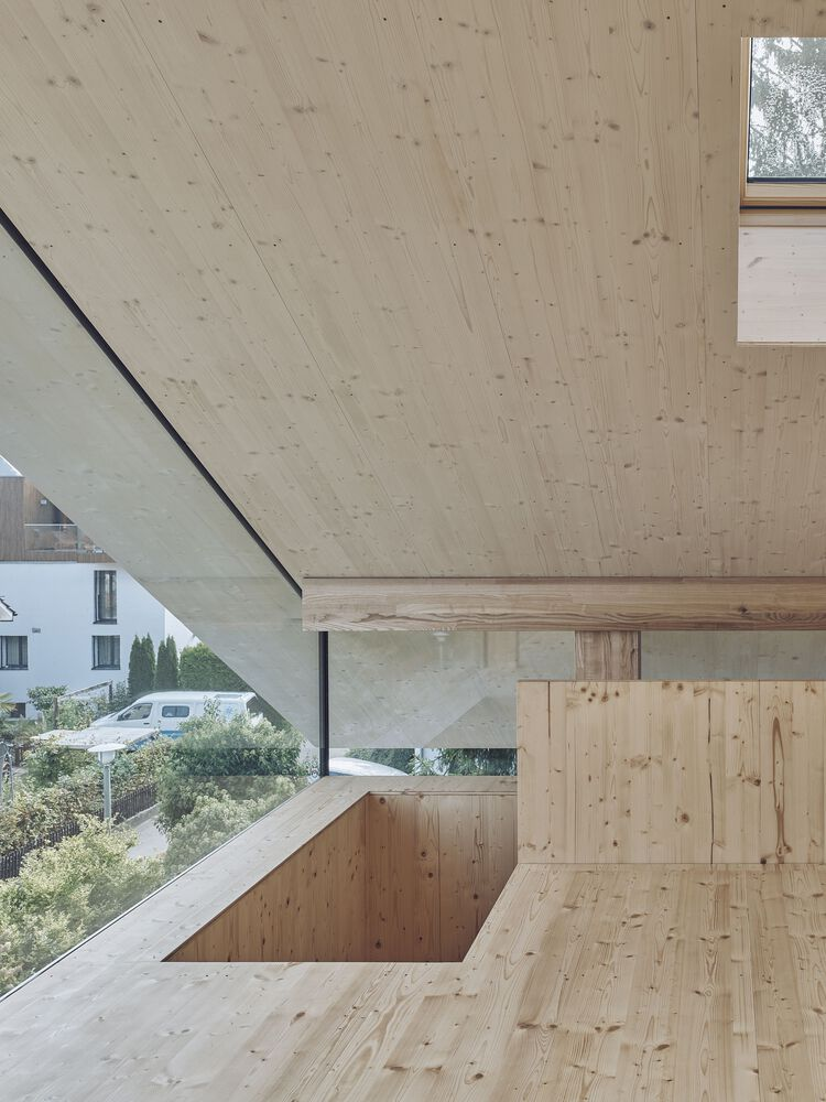 Pale timber interior with horizontal ribbon window overlooking residential buildings and greenery