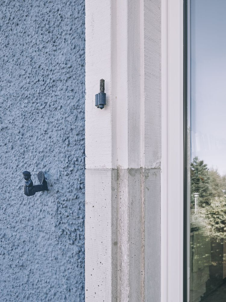 Close-up of window jamb detail showing textured stucco meeting concrete and glazing with fasteners
