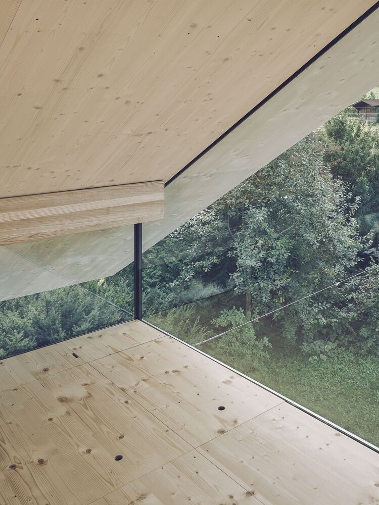Corner window detail with laminated timber ceiling extending over glass toward sloped garden beyond