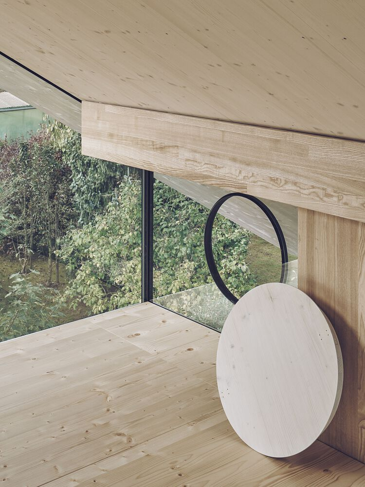 Interior corner with exposed timber beam and circular wood pendant light framing a view to garden