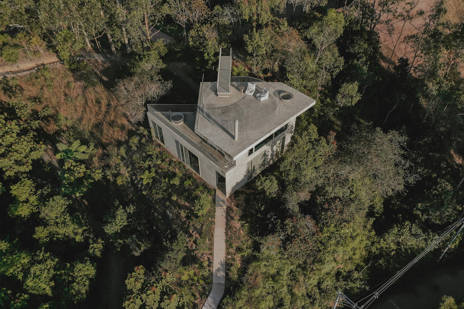 Aerial view of the concrete house with curved rooftop terrace surrounded by dense forest canopy