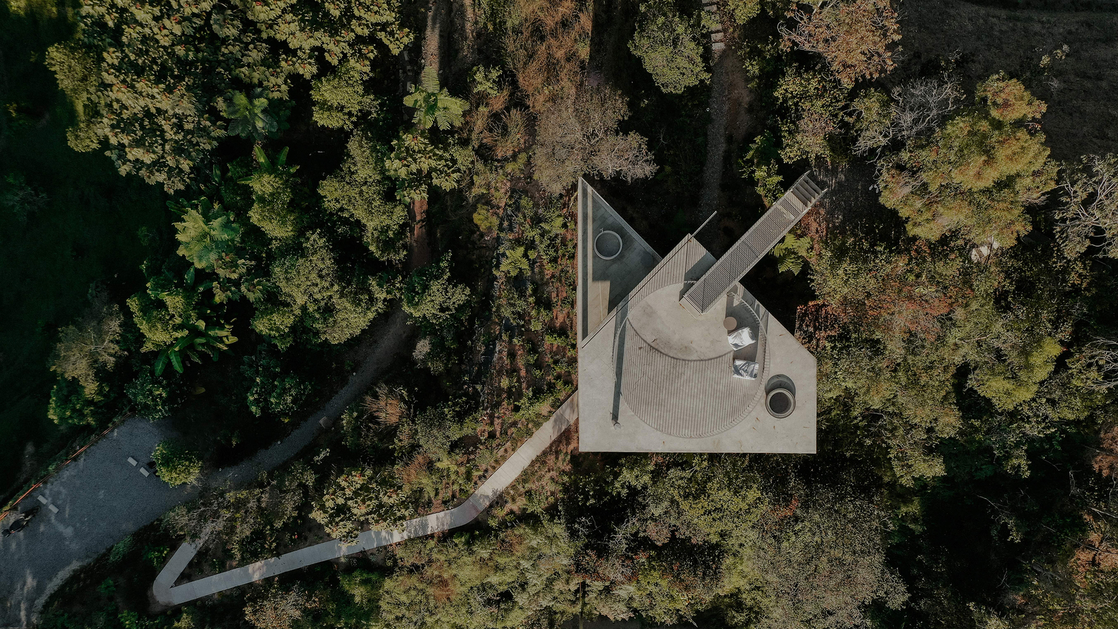 Top-down view of the curved roof terrace, circular stair tower, and winding access path through trees