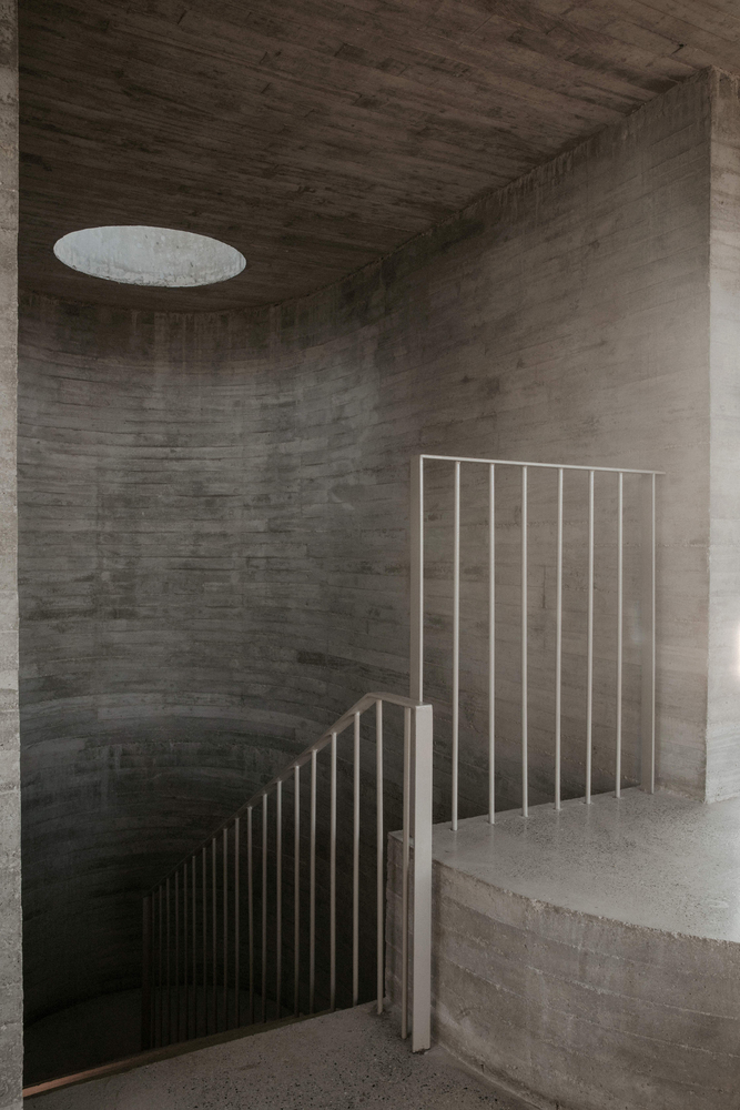 Curved concrete stairwell with vertical metal balustrade and circular skylight above board-formed walls