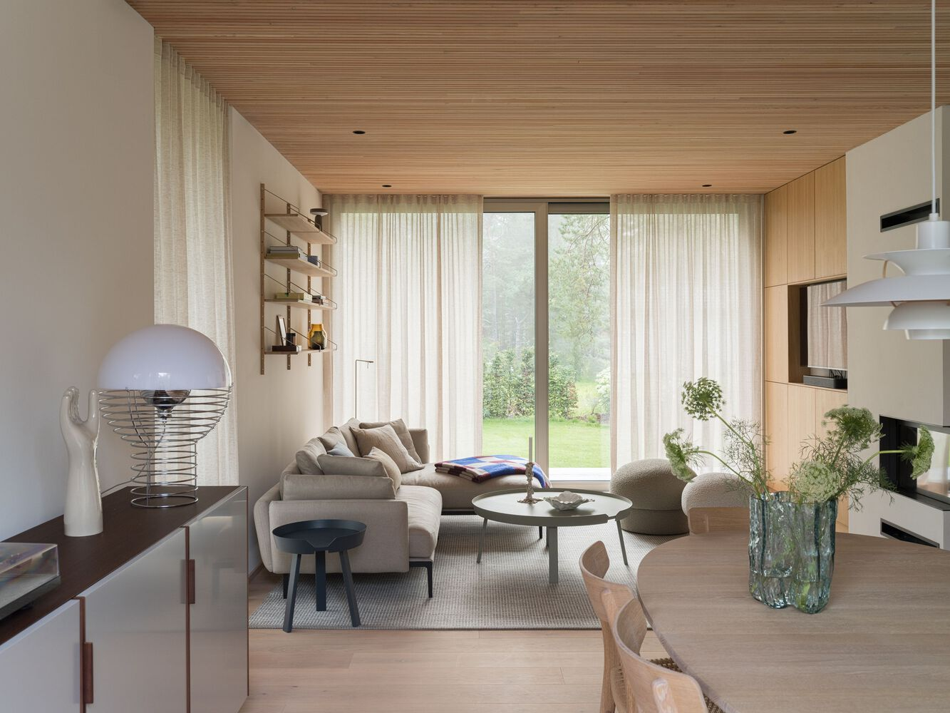 Living room with slatted timber ceiling and sheer curtains framing a view to the garden