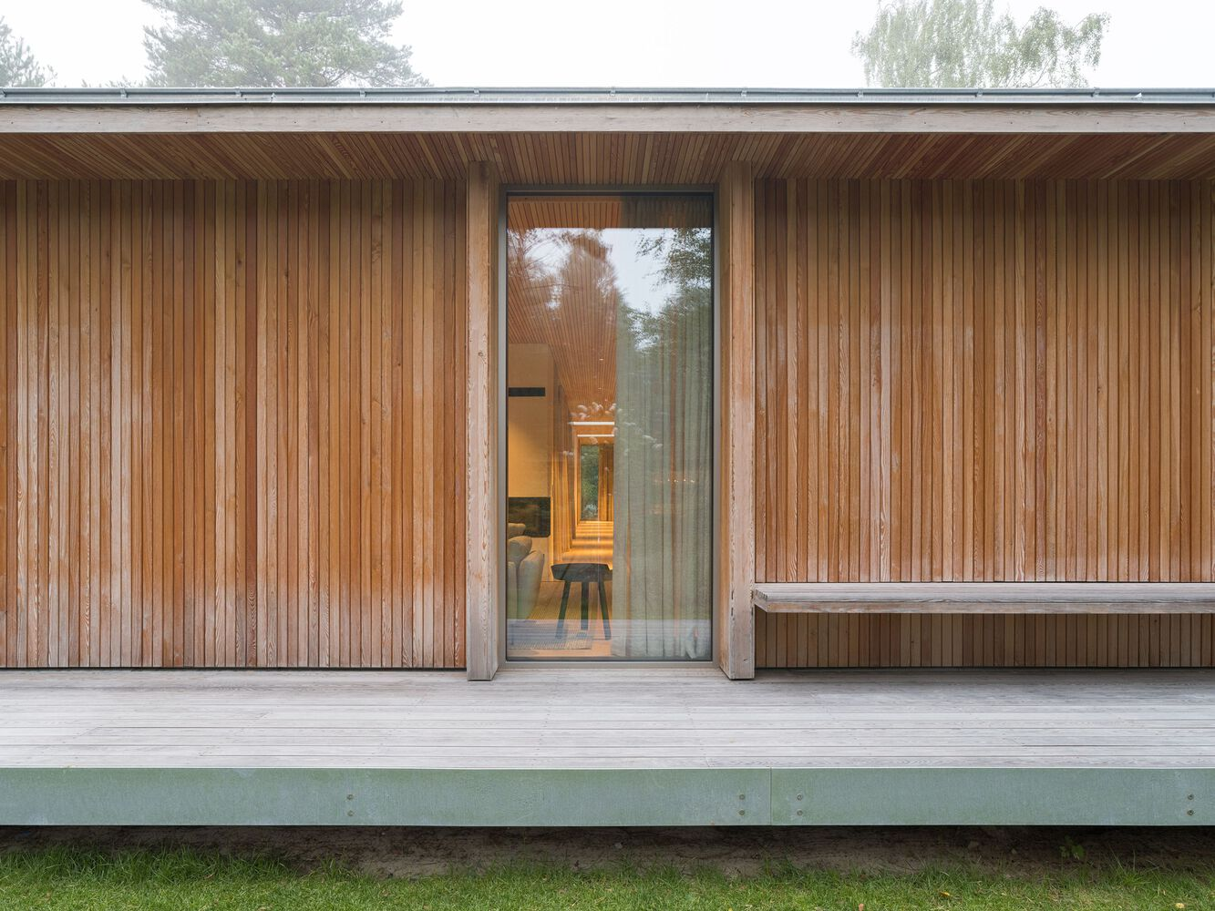 Covered terrace with vertical timber cladding and full-height glazed entry revealing interior in autumn mist