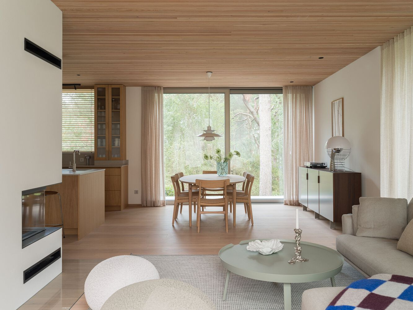 Open-plan living and dining space with timber-slatted ceiling and floor-to-ceiling windows framing garden views