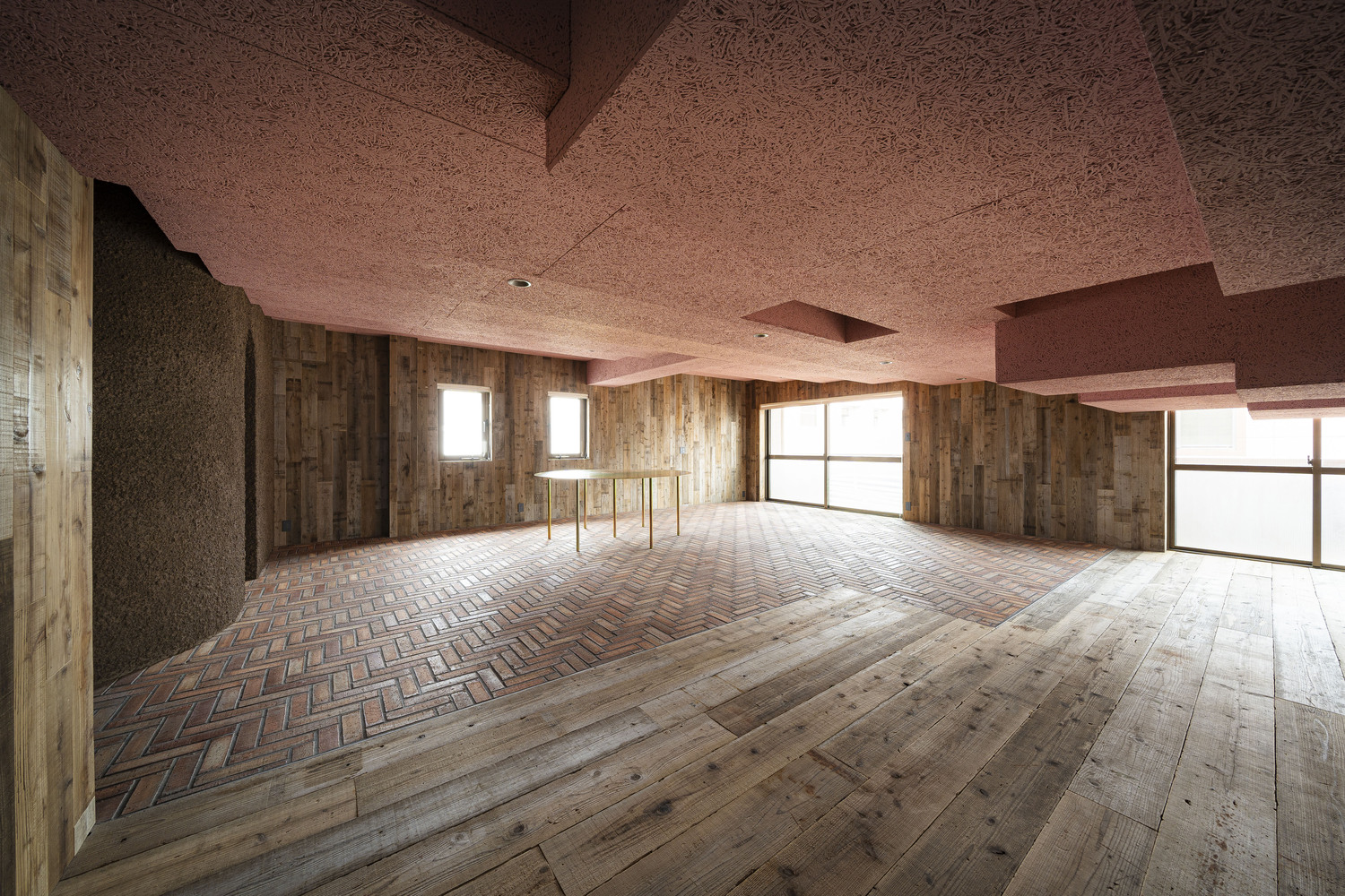 Open floor with herringbone and plank wood patterns, timber walls, pink textured ceiling and metal railing