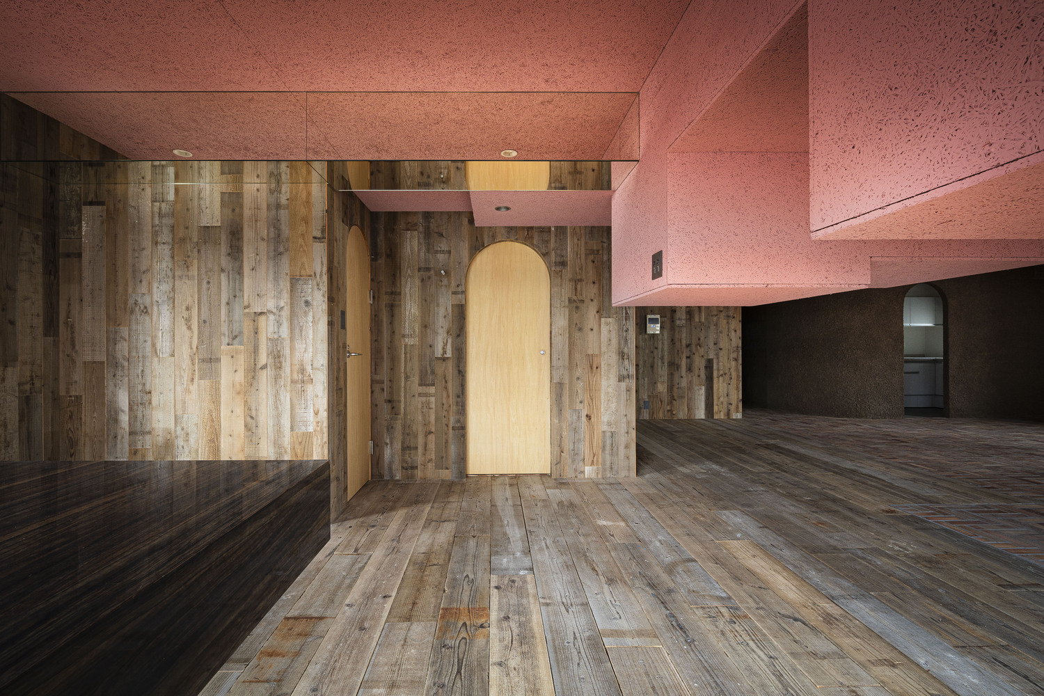Arched doorway in timber wall beneath pink textured ceiling planes and open floor beyond