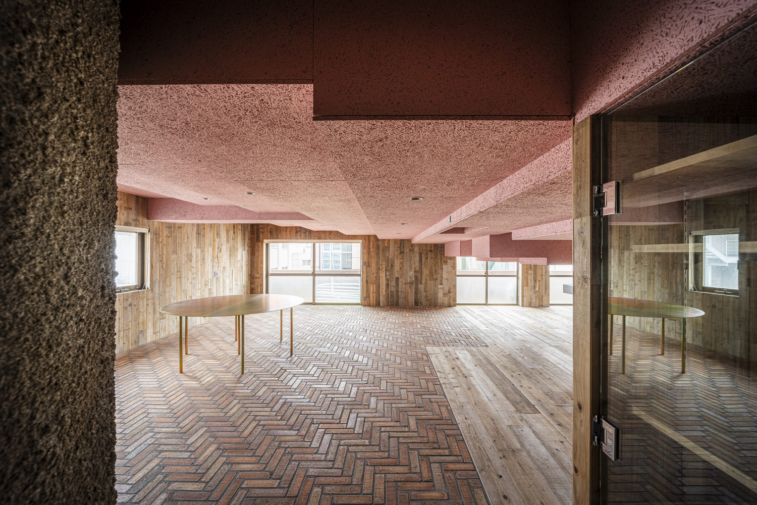 Open room with herringbone brick flooring meeting timber planks and pink cork ceiling beams overhead
