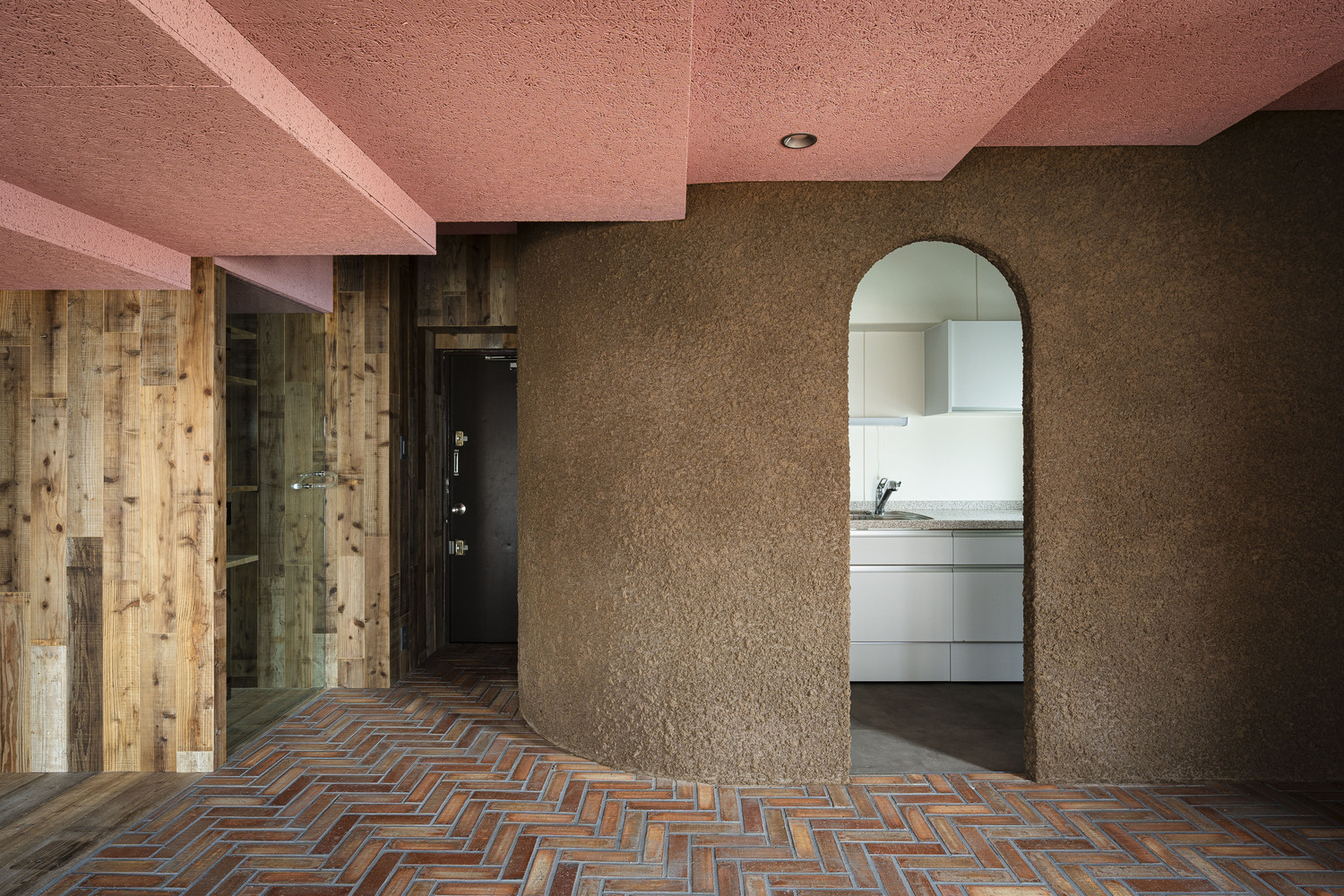 View through arched opening to kitchen with herringbone brick floor and reclaimed timber wall cladding