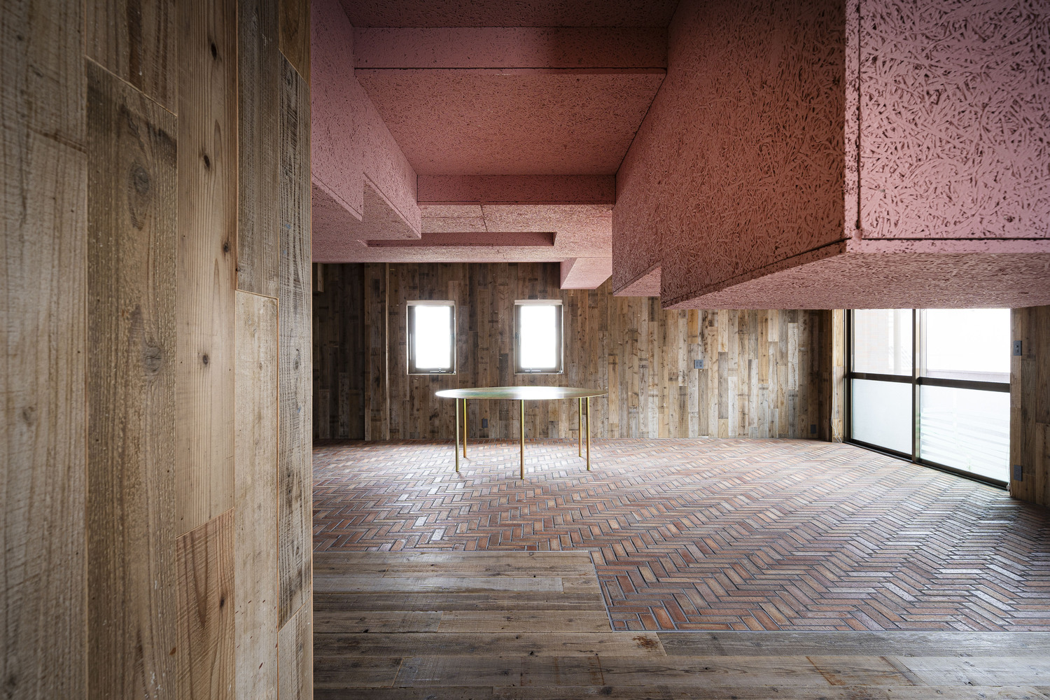 Room with brass table centered between timber walls under pink cork ceiling and clerestory windows