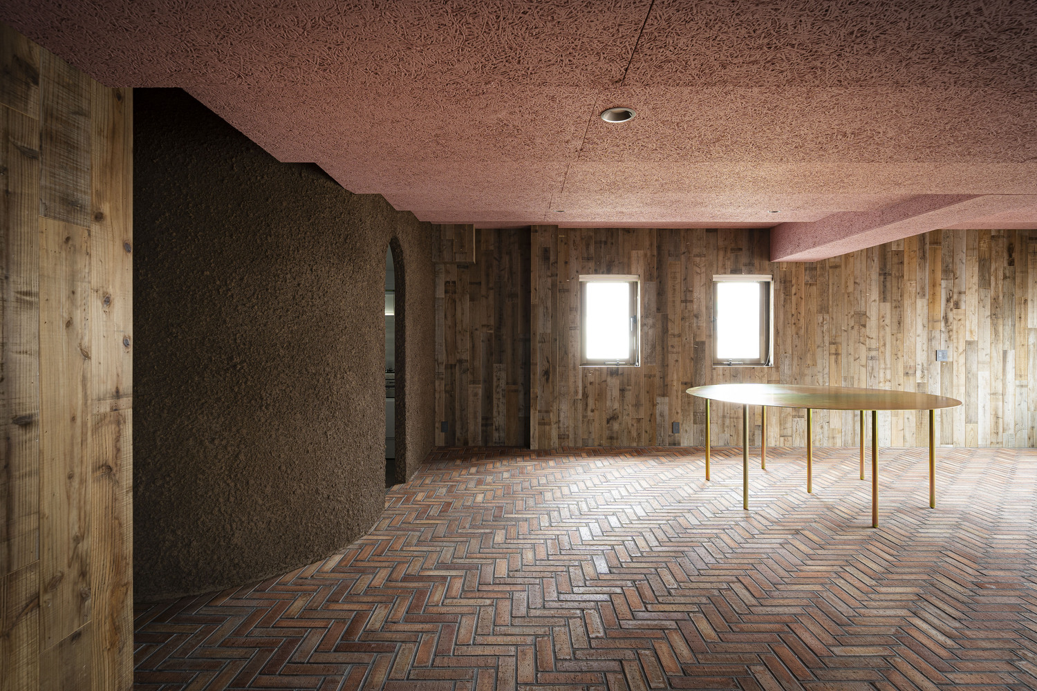 Curved partition wall in dark cork beside herringbone brick floor and brass dining table