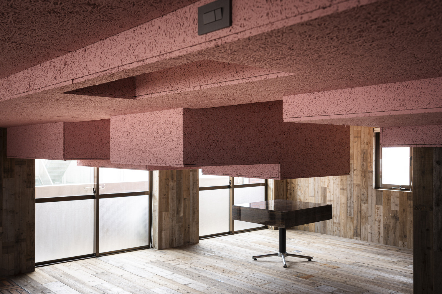 Interior room with pink textured ceiling panels and timber-clad lower walls lit by soft daylight