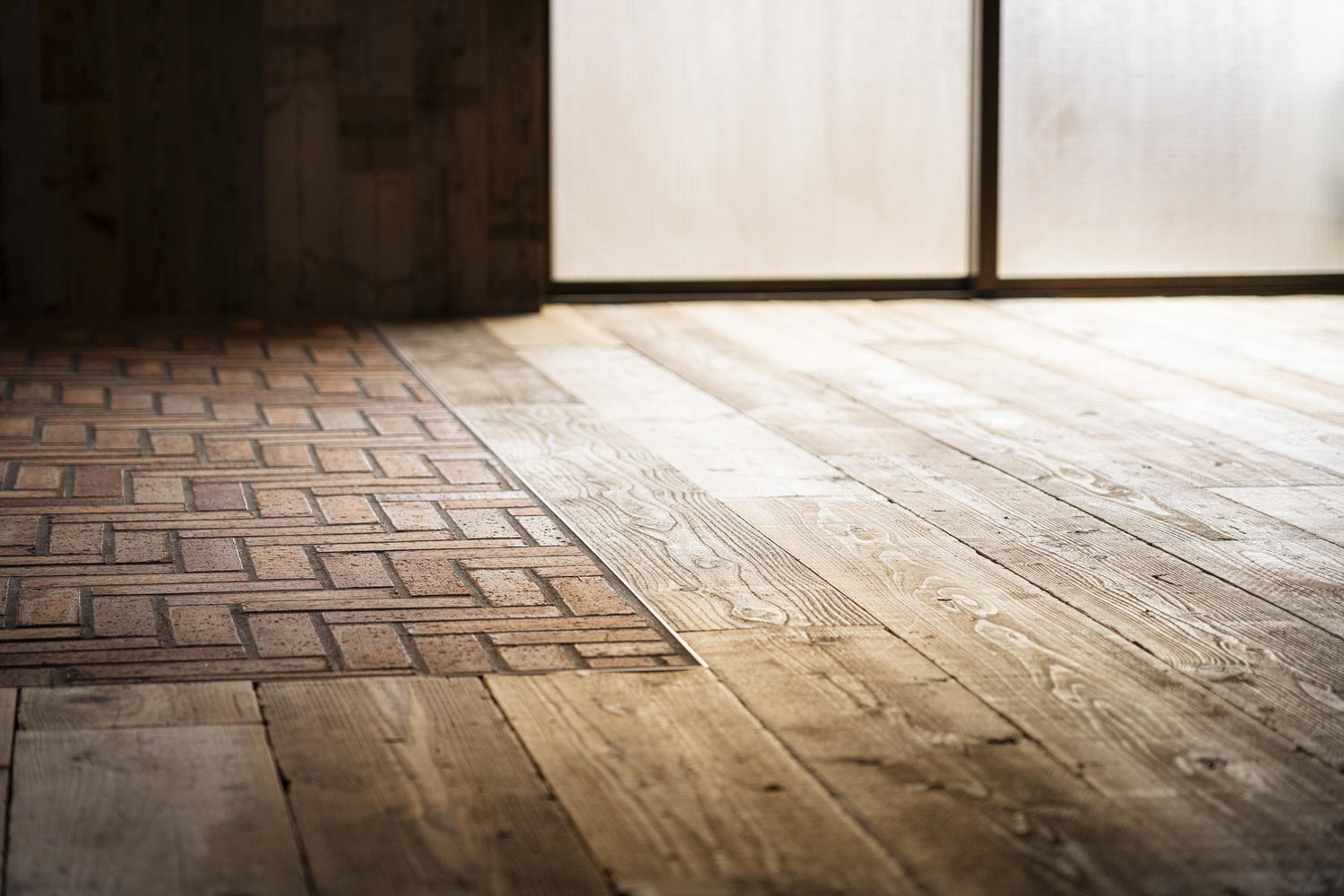 Floor transition from herringbone brick to wide timber planks near glazed wall