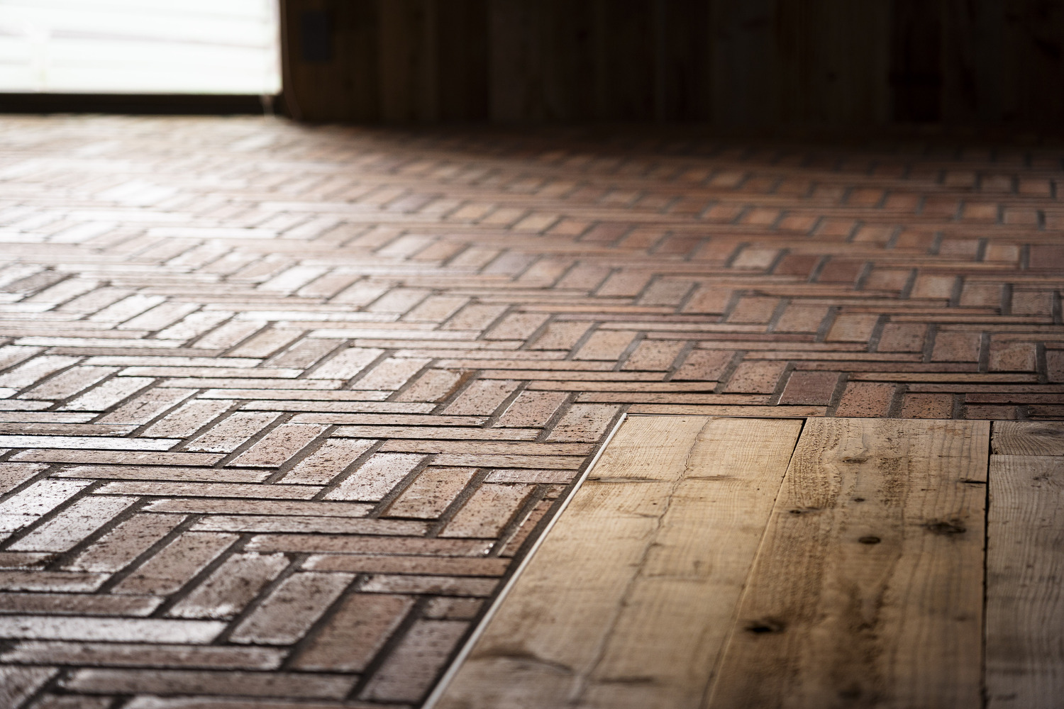 Close-up of herringbone brick flooring meeting reclaimed timber planks in bright sunlight