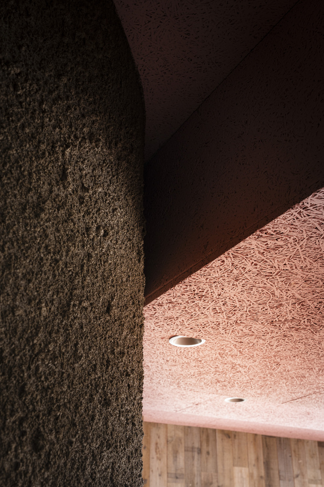 Curved dark textured wall meeting pink fibrous ceiling panel at shadow line
