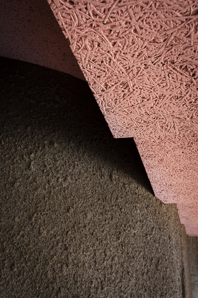 Detail of pink fibrous ceiling panel edge against dark textured wall surface