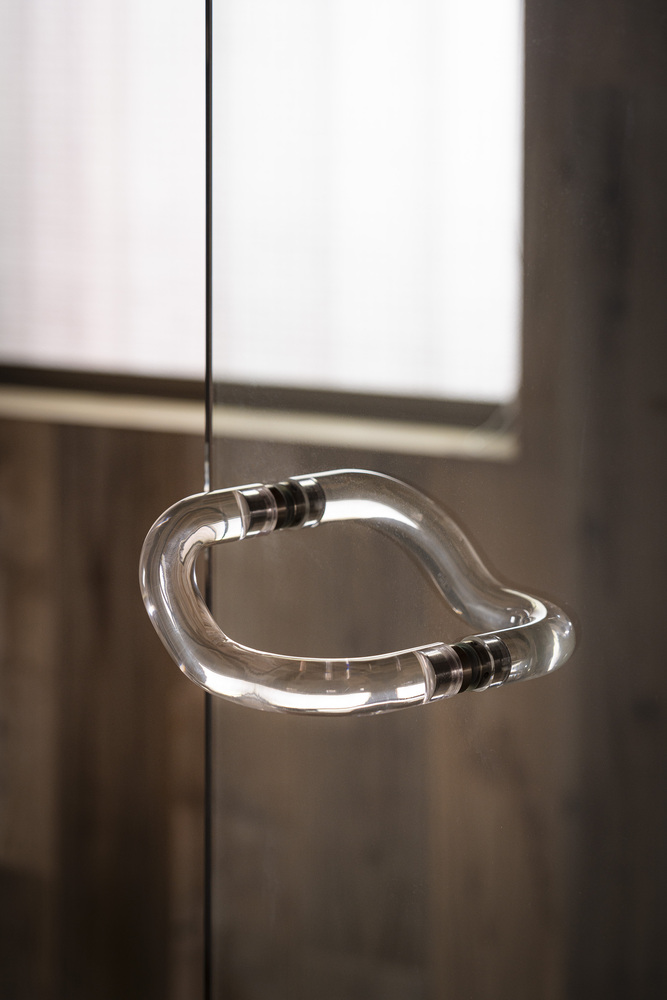 Suspended glass pendant light in an organic curved form illuminated against timber paneling
