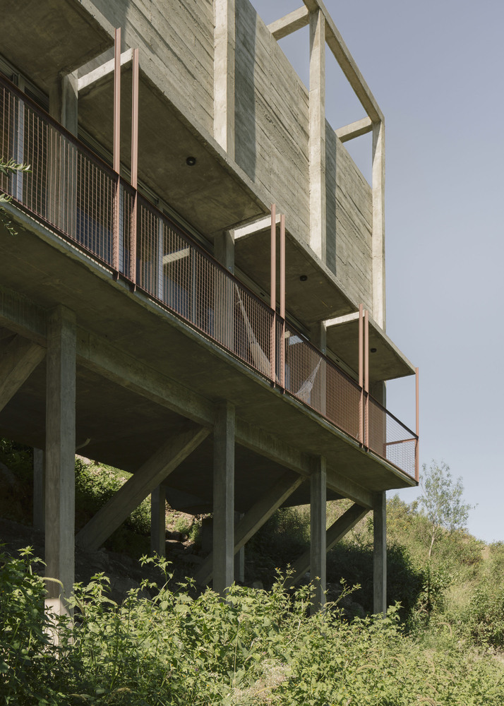 Underside view of elevated concrete structure with metal mesh balcony railings supported by angled pilotis