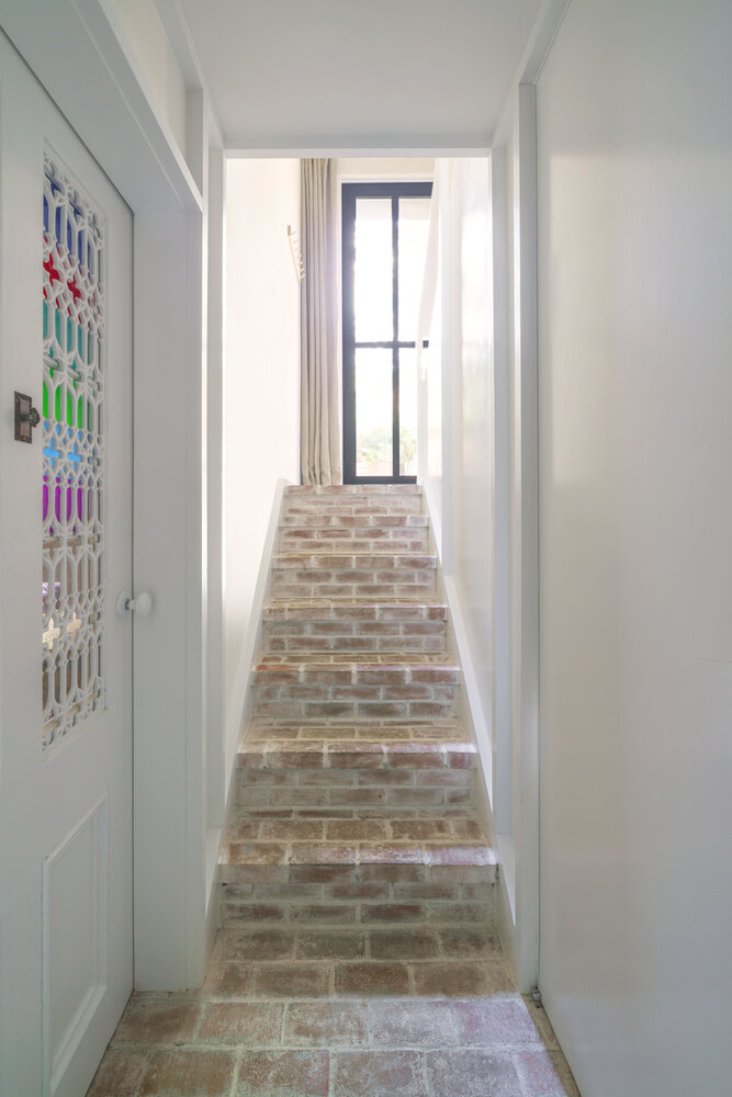 Narrow staircase with reclaimed brick treads ascending to a black-framed window at the landing