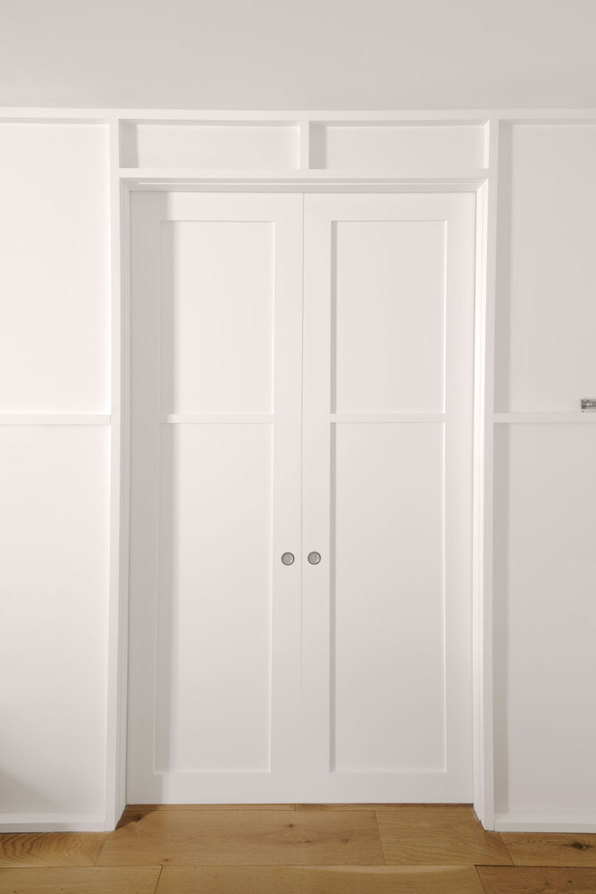White paneled closet doors with twin handles set into recessed millwork and oak flooring