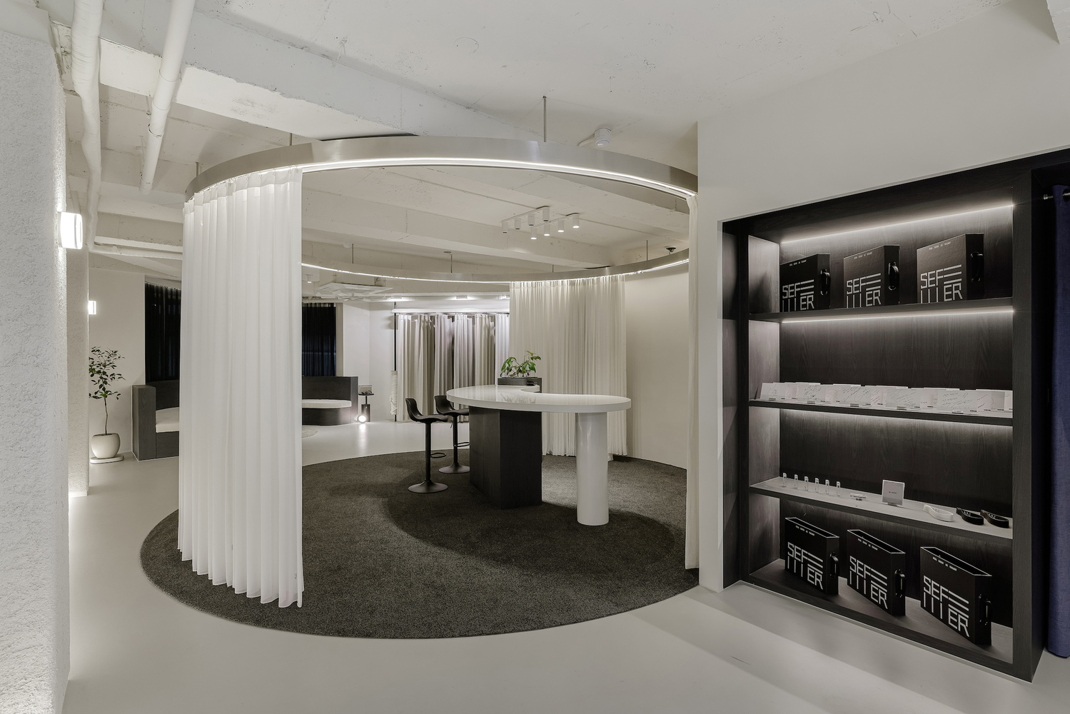 Reception area with curved white curtain screen, circular table with columns, and dark product shelving
